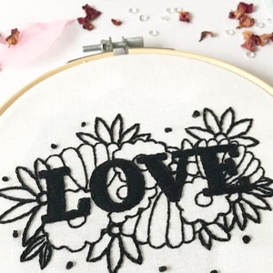 May include: Embroidered hoop art with the word "LOVE" in black lettering surrounded by black floral embroidery on a white background.