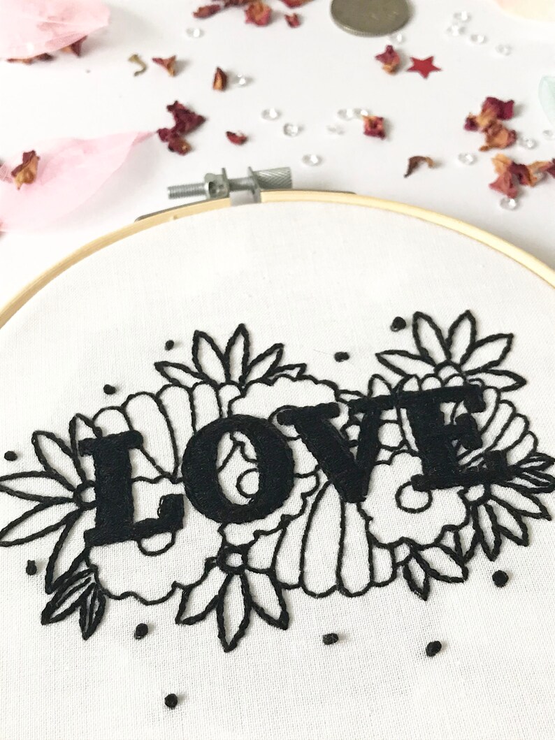 May include: Embroidered hoop art with the word "LOVE" in black lettering surrounded by black floral embroidery on a white background.