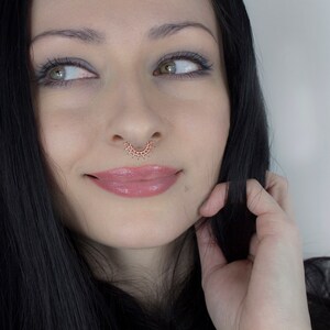 May include: A woman with long black hair and a septum piercing. She is wearing makeup and has a slight smile on her face.