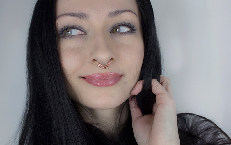 May include: A woman with long black hair and a septum piercing. She is wearing makeup and has a slight smile on her face.