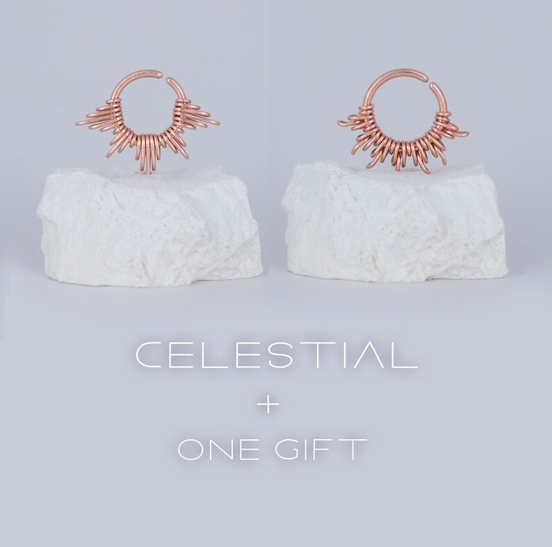 May include: Two rose gold nose rings with a sunburst design. The text "CELESTIAL + ONE GIFT" is below the rings.