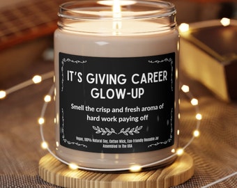 Könnte beinhalten: Eine braune Glaskerze mit einem schwarzen Etikett, auf dem "IT'S GIVING CAREER GLOW-UP" und "Smell the crisp and fresh aroma of hard work paying off" steht. Die Kerze steht auf einem Holzuntersetzer und ist von Lichterketten umgeben.