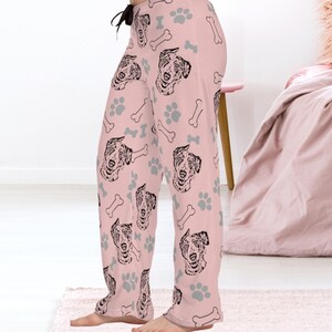 Op de afbeelding: Roze pyjamabroek met een herhalend patroon van zwart-witte Australian Shepherd hondenkoppen, grijze voetafdrukken en witte botvormen.