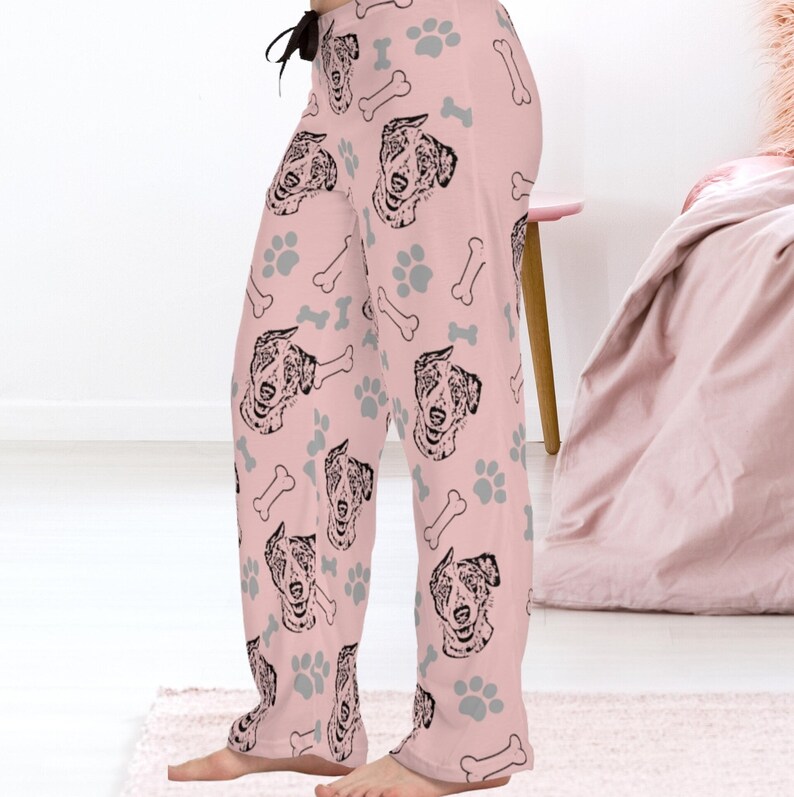 Op de afbeelding: Roze pyjamabroek met een herhalend patroon van zwart-witte Australian Shepherd hondenkoppen, grijze voetafdrukken en witte botvormen.