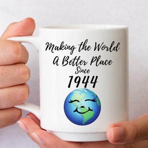 May include: White ceramic mug with black text that reads "Making the World a Better Place Since 1944". A cartoon image of a smiling earth is below the text.