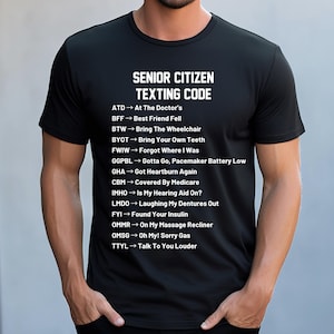 May include: A black short-sleeved t-shirt featuring white text that reads Senior Citizen Texting Code followed by a list of humorous acronym definitions including ATD, BFF, BTW, BYOT, FWIW, GGPBL, GHA, CBM, IMHO, LMDO, FYI, OMMR, OMSG, and TTYL.