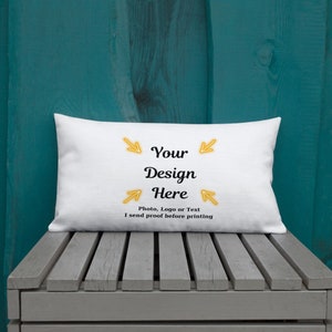 K&ouml;nnte beinhalten: Ein wei&szlig;es rechteckiges Kissen mit dem Text "Your Design Here" in Schwarz, mit gelben Pfeilen, die auf den Text zeigen. Darunter steht "Photo, Logo or Text I send proof before printing". Das Kissen liegt auf einer Holzoberfl&auml;che.