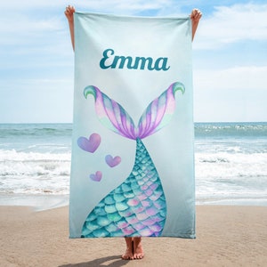 May include: A light blue beach towel with a mermaid tail design. The tail is teal, green, and purple with pink hearts. The towel has the name "Emma" printed on it.