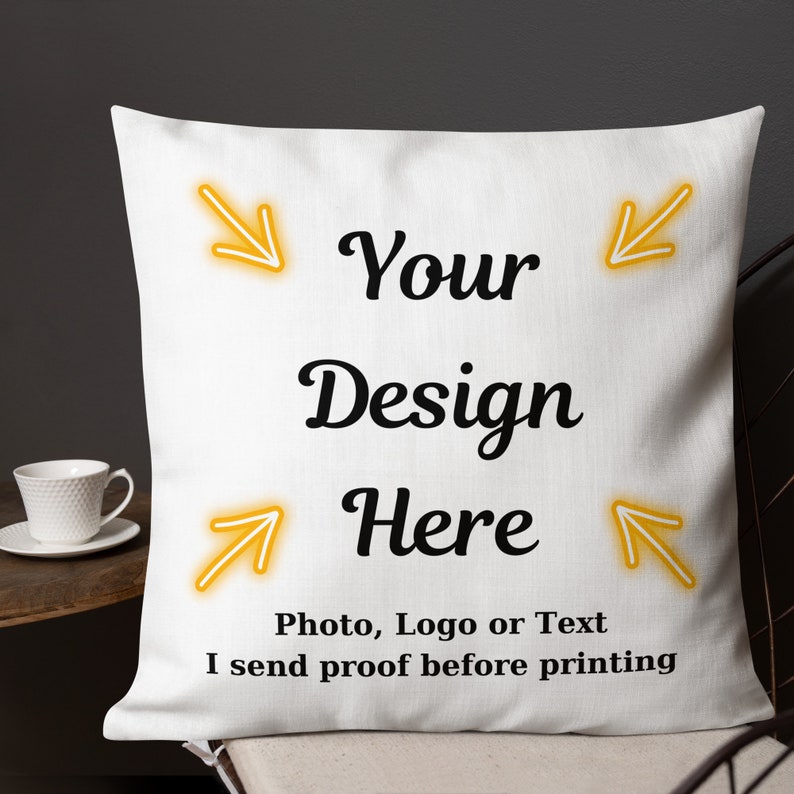 K&ouml;nnte beinhalten: Wei&szlig;es quadratisches Kissen mit dem Text "Your Design Here" in schwarzer Schrift. Das Kissen hat auch den Text "Photo, Logo or Text I send proof before printing". Gelbe Pfeile zeigen auf den Text. Eine wei&szlig;e Teetasse ist im Hintergrund zu sehen.