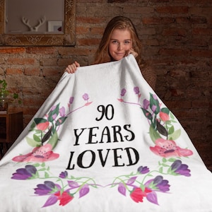 May include: White throw blanket with a floral design and the text "90 Years Loved".