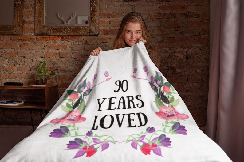 May include: White throw blanket with a floral design and the text "90 Years Loved".