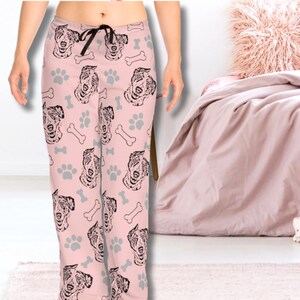 Op de afbeelding: Roze pyjamabroek met een herhalend patroon van zwarte en witte hondenkoppen en potafdrukken.