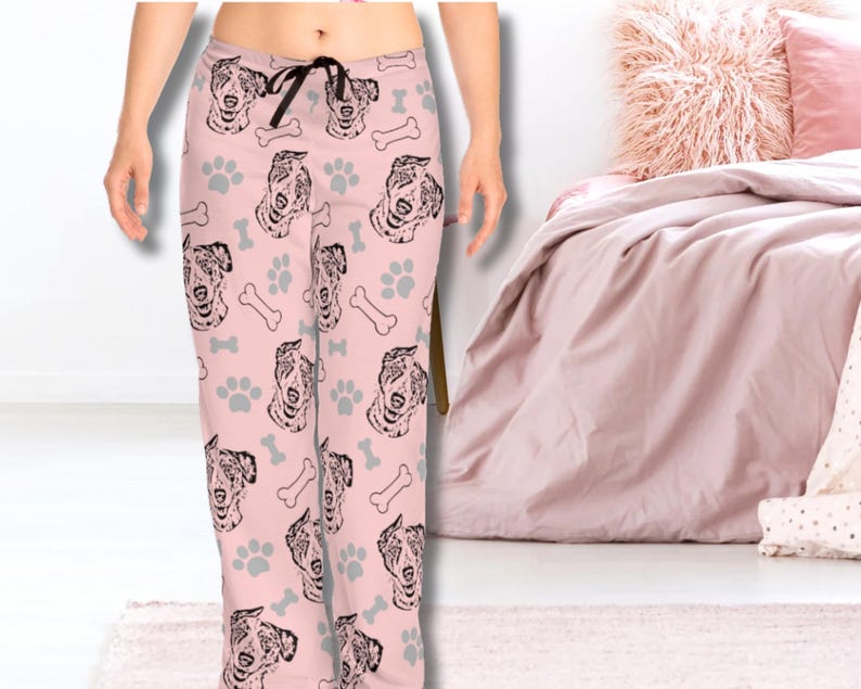 Op de afbeelding: Roze pyjamabroek met een herhalend patroon van zwarte en witte hondenkoppen en potafdrukken.