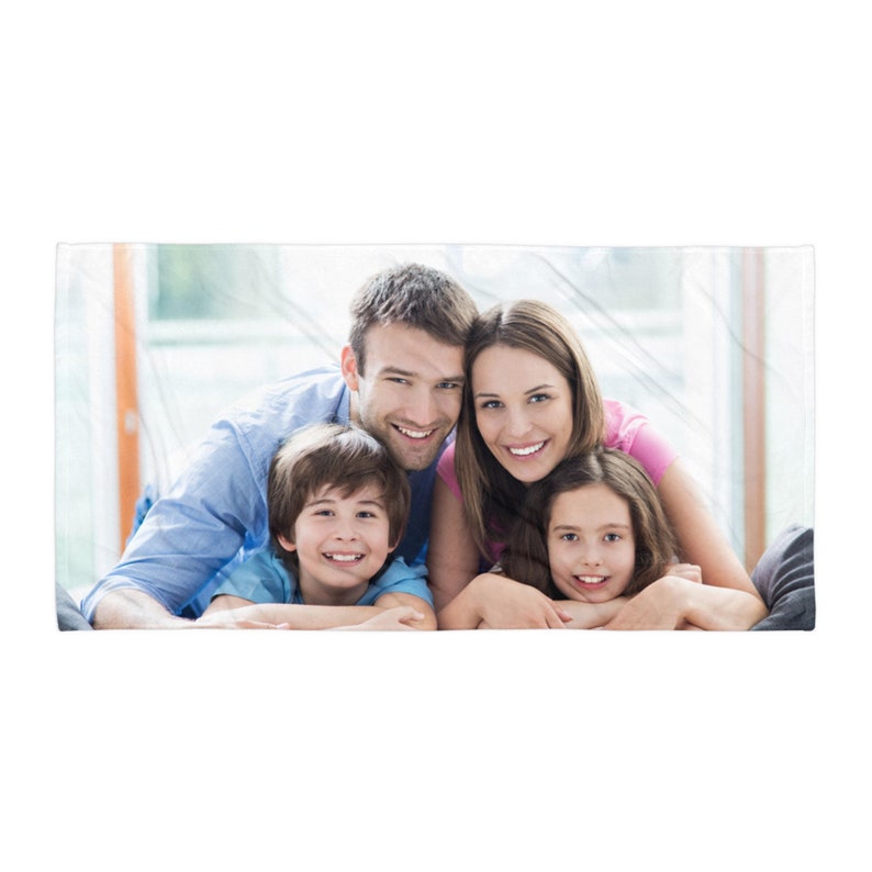 May include: A rectangular beach towel featuring a printed photograph of a family of four, including two adults and two children, all smiling and positioned closely together in a bright, indoor setting with soft natural lighting.