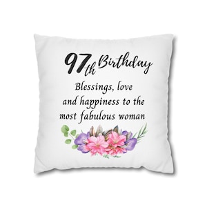 May include: White square pillow with the text "97th Birthday" in black script. Below the text is the phrase "Blessings, love and happiness to the most fabulous woman." A floral arrangement of pink and purple flowers and green leaves is at the bottom.