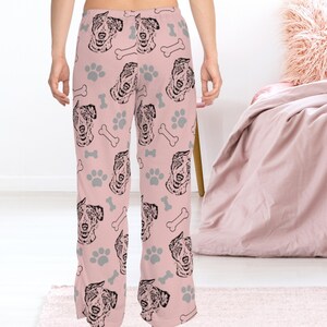 Op de afbeelding: Roze pyjamabroek met een herhalend patroon van zwart-witte Australian Shepherd hondenkoppen, poot afdrukken en botvormen.
