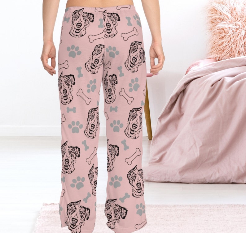 Op de afbeelding: Roze pyjamabroek met een herhalend patroon van zwart-witte Australian Shepherd hondenkoppen, poot afdrukken en botvormen.
