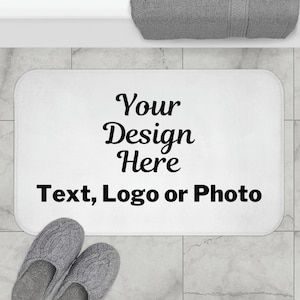 May include: White bath mat with the text "Your Design Here Text, Logo or Photo" printed in black.