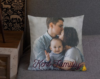 Könnte beinhalten: Ein weißes Kissen mit einem Foto einer dreiköpfigen Familie. Das Foto zeigt einen Mann, der eine Frau auf die Stirn küsst, während er ein Baby in seinen Armen hält. Der Text "Kent Family" ist in Kursivschrift am unteren Rand des Kissens geschrieben.