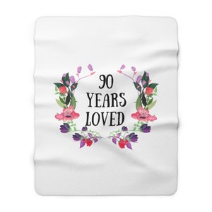 May include: White throw blanket with a floral wreath design and the text "90 Years Loved" in black.
