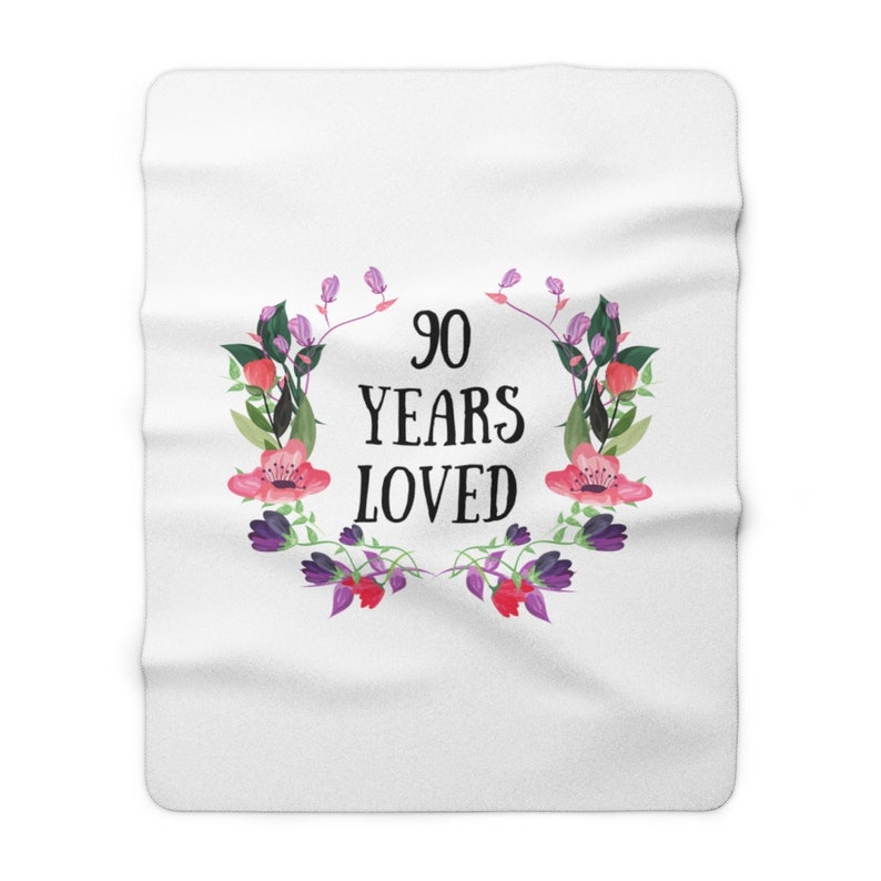 May include: White throw blanket with a floral wreath design and the text "90 Years Loved" in black.