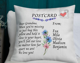 May include: White pillow with a postcard design featuring a message to Grandma from her grandchildren. The message reads "Dear Grandma, When you're missing us just hug this pillow and hold it close to your heart, you'll feel our love no matter how far apart we are! We love you!" The postcard is decorated with a floral design and a red heart stamp. The names of the grandchildren are listed below the message: Eva, Mila, Olivia, Madison, Benjamin.