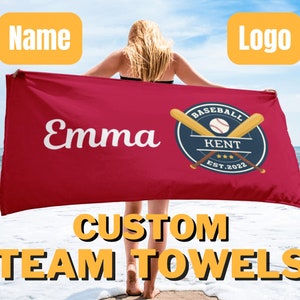 May include: A red beach towel with the name "Emma" and a baseball logo with the text "Baseball Kent Est. 2022". The towel is held by a person standing on a beach. The text "Custom Team Towels" is at the bottom of the image.