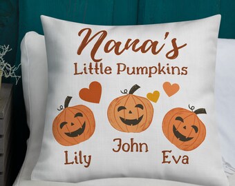 May include: White throw pillow with the text "Nana's Little Pumpkins" and three orange pumpkins with smiling faces. The pumpkins are labeled "Lily", "John", and "Eva".