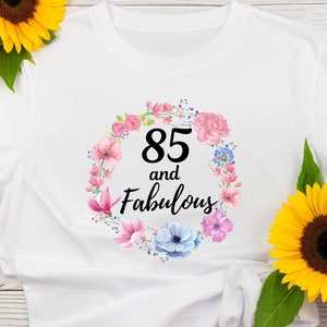 May include: White t-shirt with a floral wreath design and the text "85 and Fabulous".
