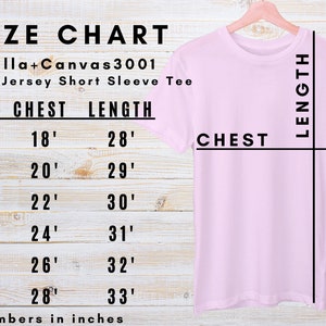 May include: A light pink Bella+Canvas 3001 unisex jersey short sleeve tee shirt hanging on a wooden hanger. A size chart shows chest and length measurements in inches: S (45.7cm chest, 71.1cm length), M (50.8cm chest, 73.7cm length), L (55.9cm chest, 76.2cm length), XL (61cm chest, 78.7cm length), 2XL (66cm chest, 81.3cm length), and 3XL (71.1cm chest, 83.8cm length).