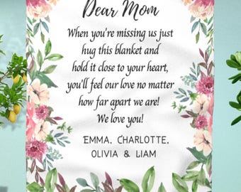 May include: A white rectangular blanket featuring a floral border of pink and peach flowers with green leaves. The text reads: Dear Mom, When you're missing us just hug this blanket and hold it close to your heart, you'll feel our love no matter how far apart we are! We love you! EMMA, CHARLOTTE, OLIVIA & LIAM.