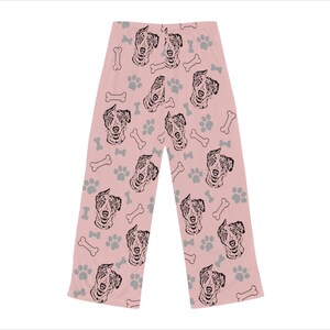 Op de afbeelding: Roze pyjamabroek met een herhalend patroon van zwart-witte Australian Shepherd hondenkoppen, botvormen en voetafdrukken.
