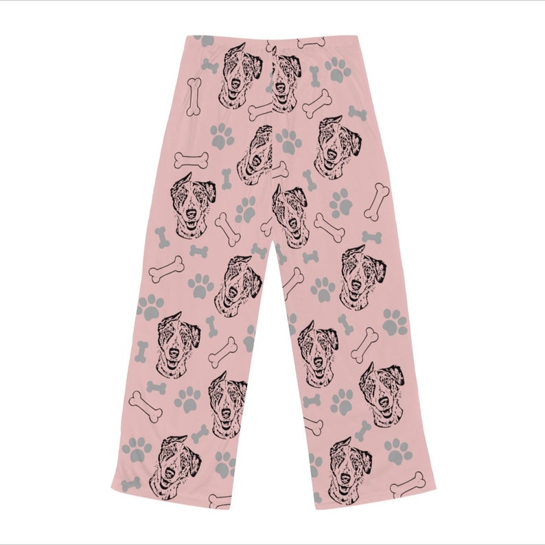 Op de afbeelding: Roze pyjamabroek met een herhalend patroon van zwart-witte Australian Shepherd hondenkoppen, botvormen en voetafdrukken.