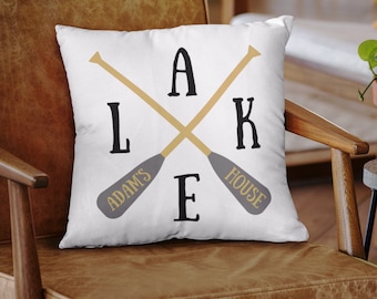 May include: White cushion with a graphic of two crossed paddles with the text "LAKE" in black letters and "ADAM'S HOUSE" in gold letters.