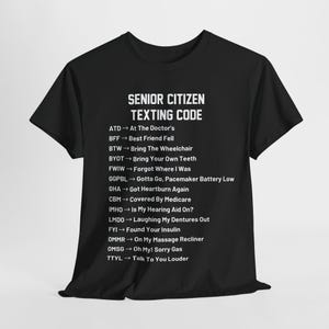 Peut inclure: T-shirt noir avec du texte blanc qui dit "Senior Citizen Texting Code" et liste des abréviations et leurs significations. Les abréviations sont liées à des expériences courantes des personnes âgées.