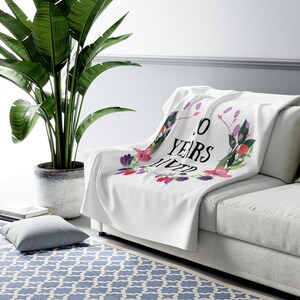 May include: White throw blanket with a floral design and the text "10 Years Lived".