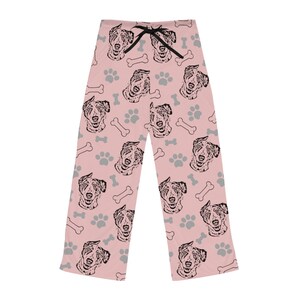 Op de afbeelding: Roze pyjamabroek met een zwart-wit patroon van gezichten van Australian Shepherd honden, voetafdrukken en botten.
