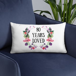 May include: White cushion with a floral design and the text "80 Years Loved".