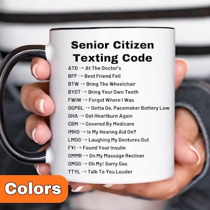 May include: A white ceramic mug with a black handle and rim, featuring the text "Senior Citizen Texting Code" and a list of abbreviations with their meanings. The mug also has the text "8 Colors" at the bottom.