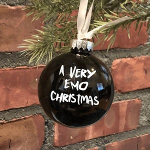 May include: A black Christmas ornament with white lettering that reads "A Very Emo Christmas".