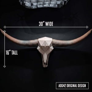 May include: A geometric bull skull wall mount with long, curved horns. The skull features a faceted, light-colored surface. Text on the image indicates dimensions of 30 inches wide and 16 inches tall, with the label ADG42 ORIGINAL DESIGN.
