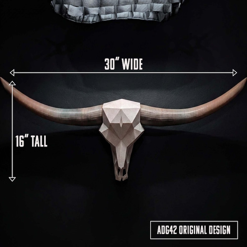 May include: A geometric bull skull wall mount with long, curved horns. The skull features a faceted, light-colored surface. Text on the image indicates dimensions of 30 inches wide and 16 inches tall, with the label ADG42 ORIGINAL DESIGN.