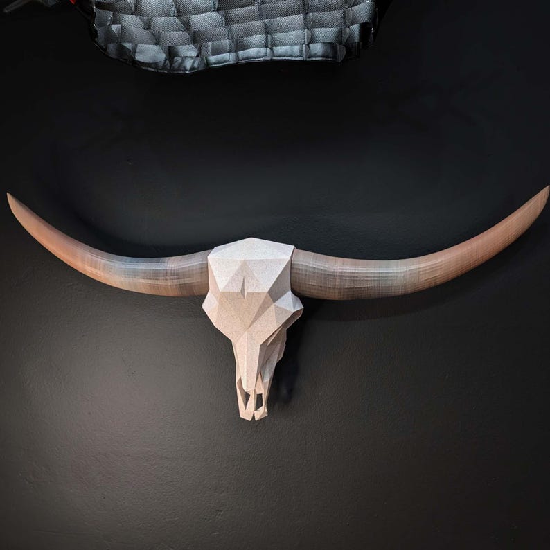 May include: A geometric bull skull wall mount featuring a light beige, speckled, low-poly cranium with long, smooth, curved horns that transition from a light tan at the base to a darker brown at the pointed tips, creating a sharp, angular aesthetic.