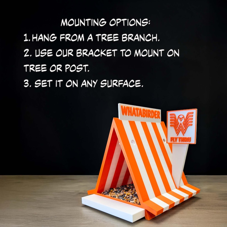May include: A triangular bird feeder with orange and white stripes, featuring the text WHATABIRDER and a logo with a bird and the text FLY THRU. The text MOUNTING OPTIONS: 1. HANG FROM A TREE BRANCH. 2. USE OUR BRACKET TO MOUNT ON TREE OR POST. 3. SET IT ON ANY SURFACE. is visible.
