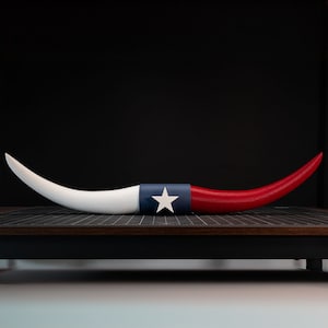 May include: A white and red bull horn with a blue and white Texas flag design. The horn is curved and has a white star in the center of the flag.