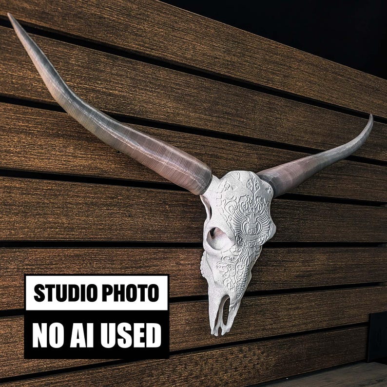 May include: A white longhorn steer skull featuring intricate carved patterns on the forehead and long, curved, grey-toned horns. The skull is mounted on a dark brown horizontal slatted wall. A black and white sign reads STUDIO PHOTO NO AI USED.