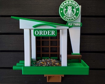 May include: A green and white bird feeder shaped like a coffee shop, with the text "Starbirds Coffee" on a sign. The feeder has a green roof, a brown bench, and the word "ORDER" on the front.