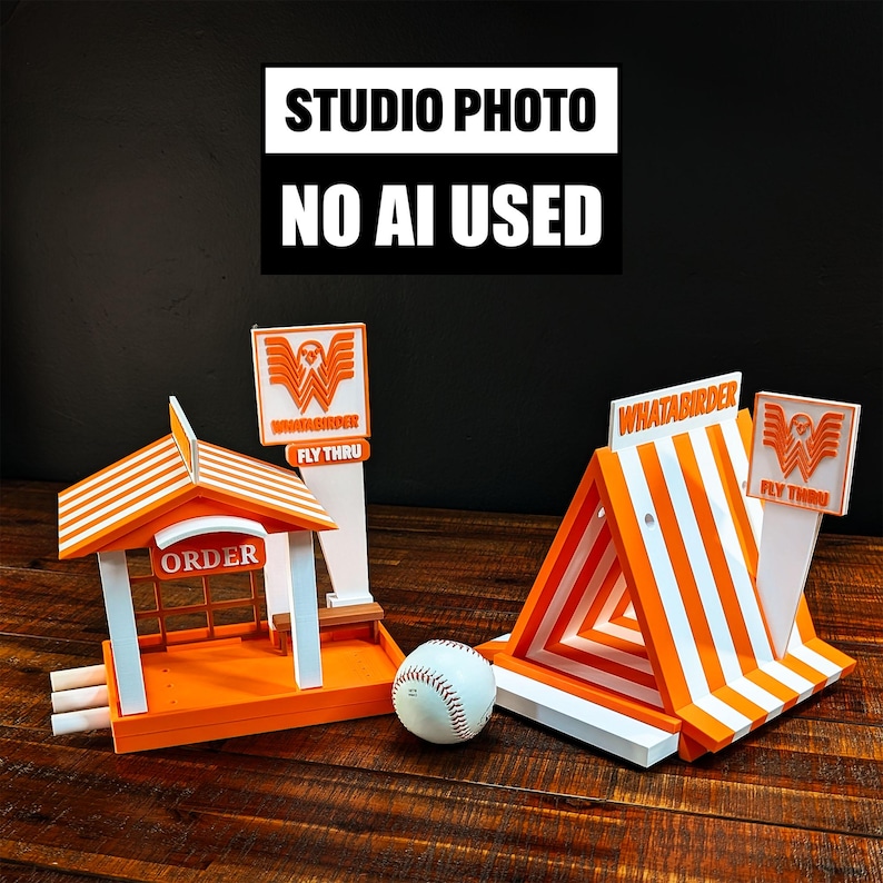May include: Two orange and white plastic miniature structures featuring the text "WHATABIRDER" and "FLY THRU" with an "ORDER" sign, accompanied by a white baseball. The structures have striped roofs and signage, with one building-style and one A-frame design.