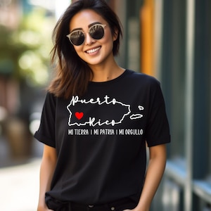 Puede incluir: Camiseta negra con un contorno blanco de Puerto Rico y las palabras "Puerto Rico" y "Mi tierra, mi patria, mi orgullo". Un coraz&oacute;n rojo est&aacute; dentro del contorno de la isla.