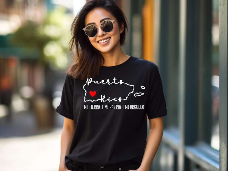 Puede incluir: Camiseta negra con un contorno blanco de Puerto Rico y las palabras "Puerto Rico" y "Mi tierra, mi patria, mi orgullo". Un coraz&oacute;n rojo est&aacute; dentro del contorno de la isla.